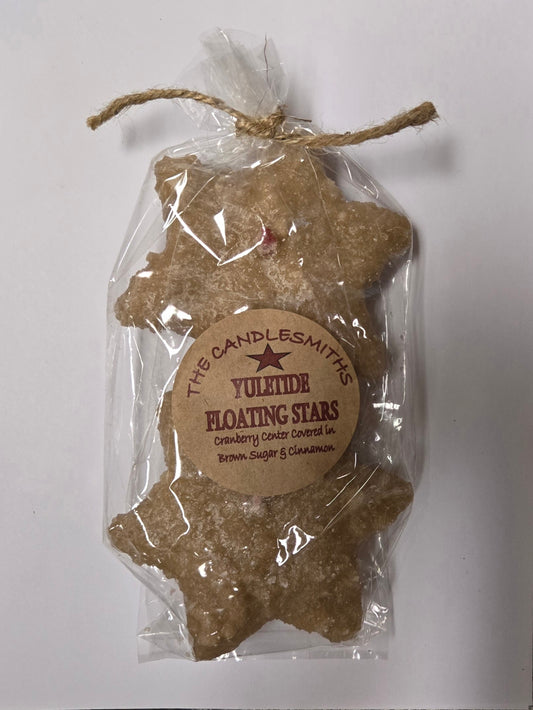 Two small star-shaped floating candles with cranberry center, dipped in brown sugar frosting, packaged in clear plastic wrapping with a twine tie and a label.